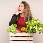 Farmer with freshly picked vegetables in a box isolated on beige background shouting with mouth wide open
